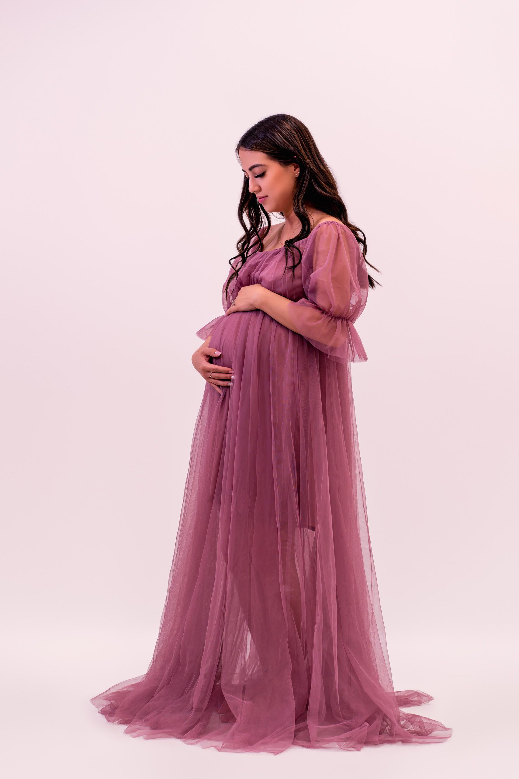 Studio maternity portrait of an expectant mother in a mauve tulle dress cradling her baby bump